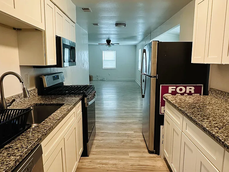 Galley kitchen with granite counters, white cabinetry, stainless appliances, and easy flow into the adjacent living area.