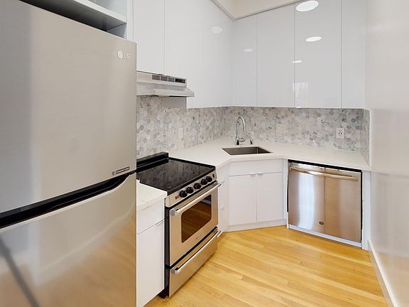 Modern kitchen with stainless steel fridge, stove, and dishwasher. Cabinets and wood flooring create a sleek, minimalist look.