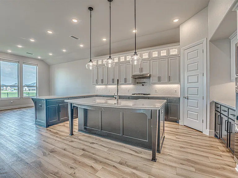 Open-concept kitchen with wood-finish flooring, a central island featuring pendant lighting, and a secondary island