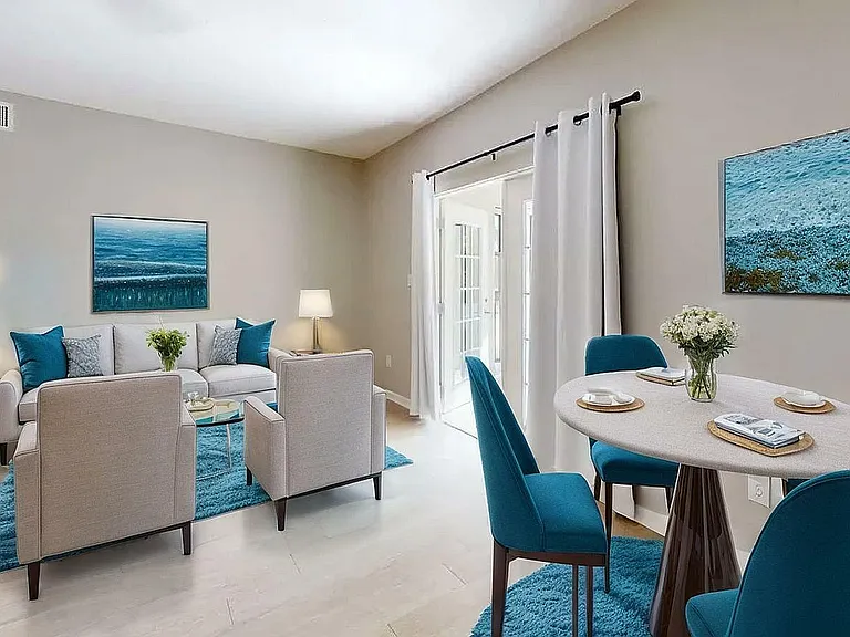 Bright, modern apartment interior featuring a stylish living room with a cozy seating area, blue accent decor, and a light-filled dining space with elegant furnishings.