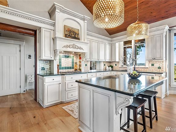 The kitchen features newer appliances including a 4 burner Wolf gas stove, double ovens, antiqued custom cabinetry with dentil molding, slab granite, huge island with breakfast bar seating and beautiful water views. 