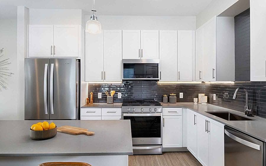 Phase II Finish Package III Kitchen with white cabinetry, grey quartz countertops, grey tile backsplash, stainless steel appliances, and hard surface flooring