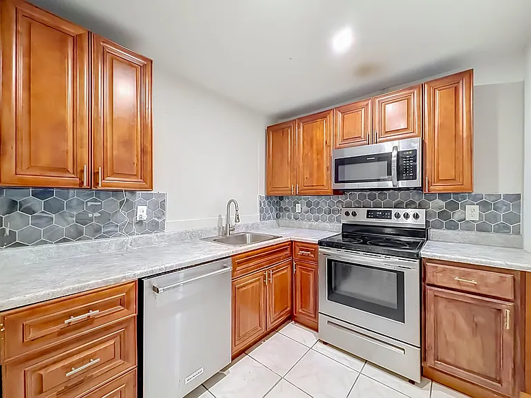 Efficient U-shaped kitchen with ample wood cabinetry, hex-tile backsplash, and stainless appliances including range and micro