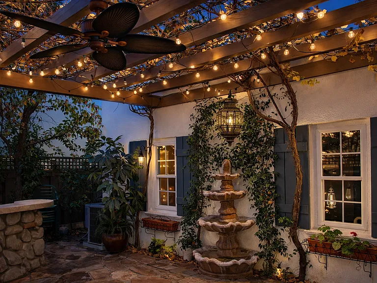 Charming covered patio with pergola, ambient lighting, and tranquil fountain creating a private outdoor retreat