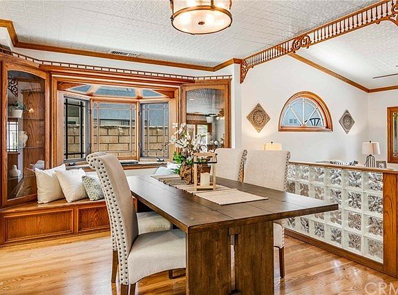 Great room includes a dining area that features a custom Bay window with granite shelf and built-in window seat with storage, lighted curio cabinets on either side, plate rail, fret work and high end ceiling with stamped metal design and powder coated white