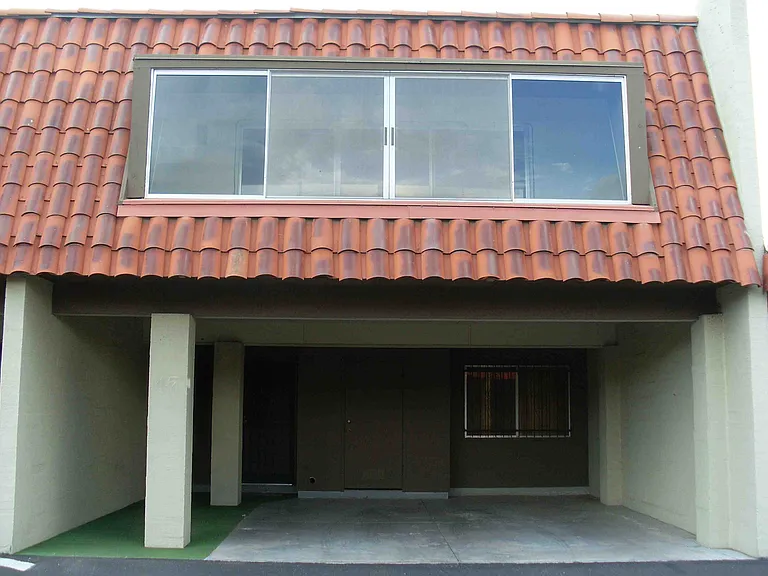 Frontal view of townhome with 2-car carport and storage closet. Windows of master bedroom enclosed balcony on 2nd floor, above.