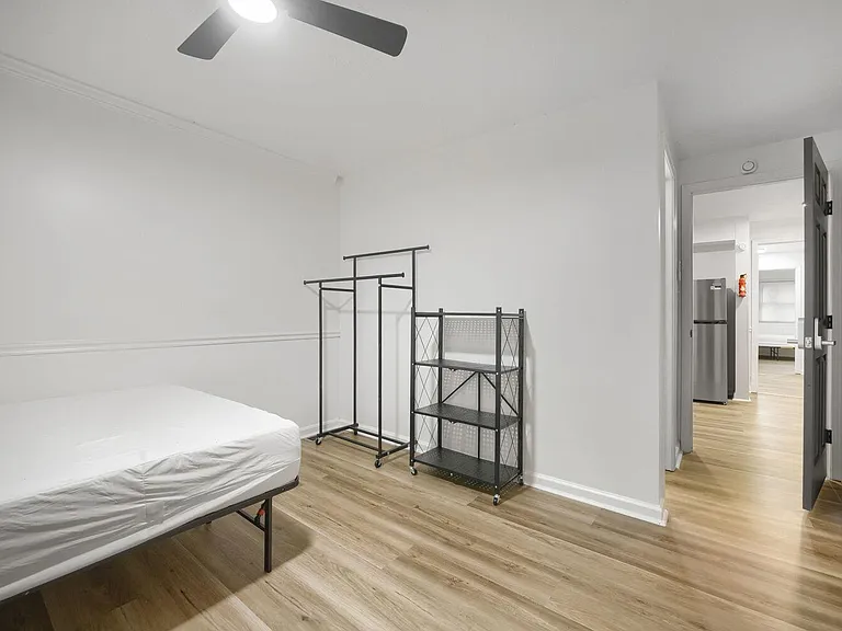 Private bedroom with wood-look flooring, ceiling fan, and space for a full bed plus open shelving and a garment rack.