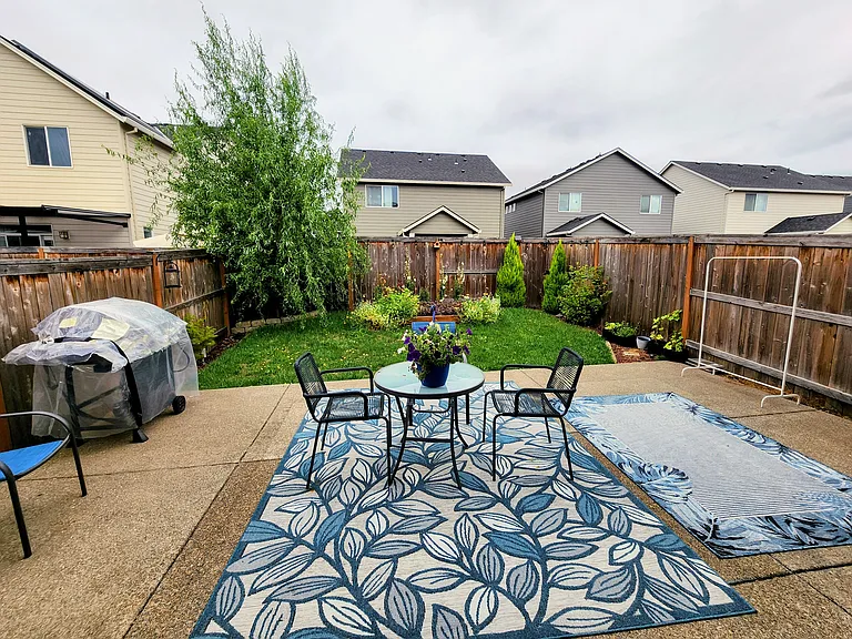 Fully fenced backyard with patio seating area, lush lawn, fully grown trees, and established garden beds