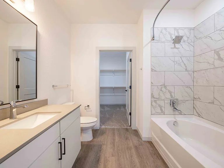 The bathroom in this Garrett Parker A1 floor plan includes a marble tiled tub and shower combo and connects directly to a walk-in closet.