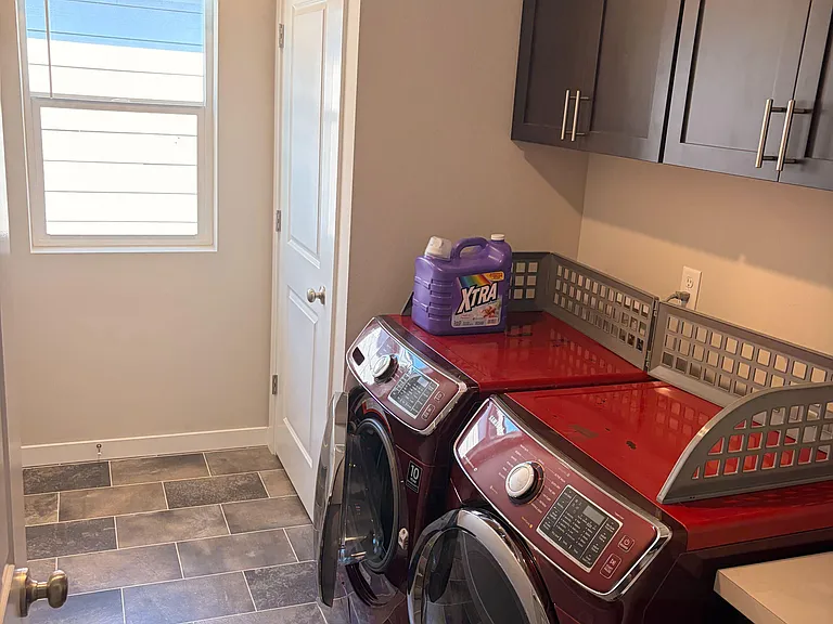 Dedicated laundry room with side-by-side washer/dryer, overhead cabinets, and a window for ventilation and light.