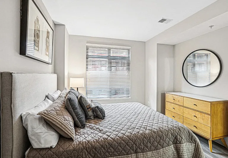 Apartment Bedroom Featuring Wood Dresser and Wall-Mounted Mirror