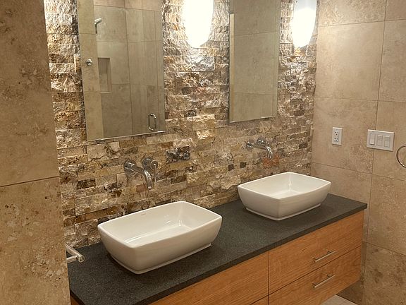 Gorgeous vanity area with custom cherry drawers, granite counter and broken faced natural stone back wall, and elegant wall sconces.