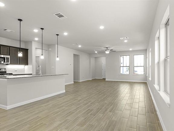 11_Unfurnished living room with light wood-style floors, visible vents, a sink, and a ceiling fan