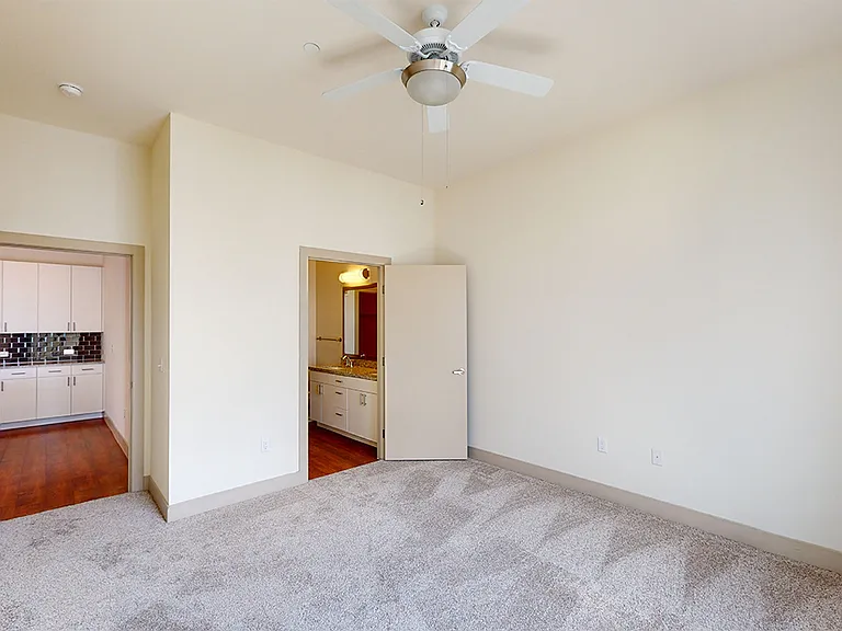 Spacious apartment bedroom with large closet, attached bathroom and plush carpet flooring.