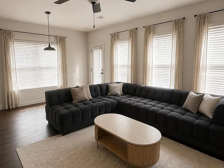 Spacious living room with a large sectional, ceiling fan, and multiple windows with blinds and drapery for flexible light con