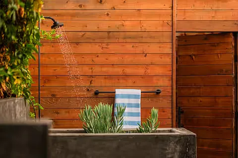 Private outdoor shower with modern black fixtures, surrounded by warm wooden walls and greenery. Perfect for a refreshing rinse, offering a natural, stylish, and serene experience.