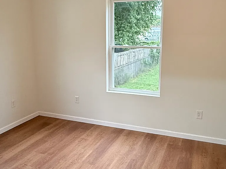 Spacious bedroom featuring two windows with installed curtain rods for plenty of natural light, a ceiling fan with light, attractive flooring, and a large walk-in closet with built-in shelving for generous storage.