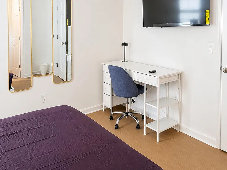 Private bedroom with dedicated desk workspace, wall-mounted TV, and full-length mirrors for added convenience.