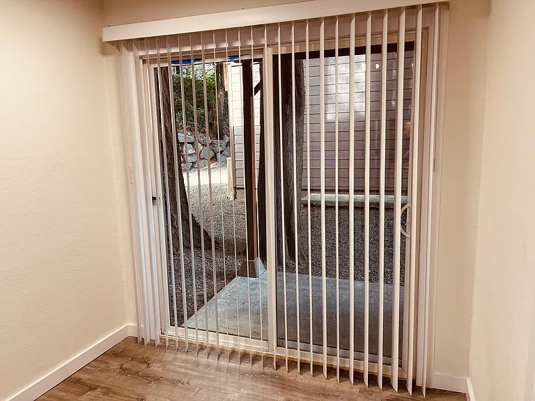 Large sliding glass door opens up to a private patio looking into a quiet backyard with trees and greenery.