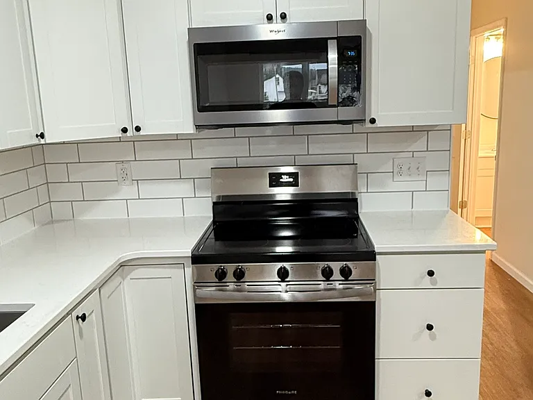 Brand-new kitchen featuring Whirlpool stainless-steel appliances, including range and built-in microwave, modern white cabinetry with ample storage, quartz-style countertops, subway-tile backsplash, and attractive new flooring.