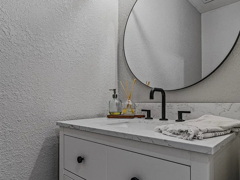 White vanity with black hardware, stone-finish countertop, and integrated rectangular sink