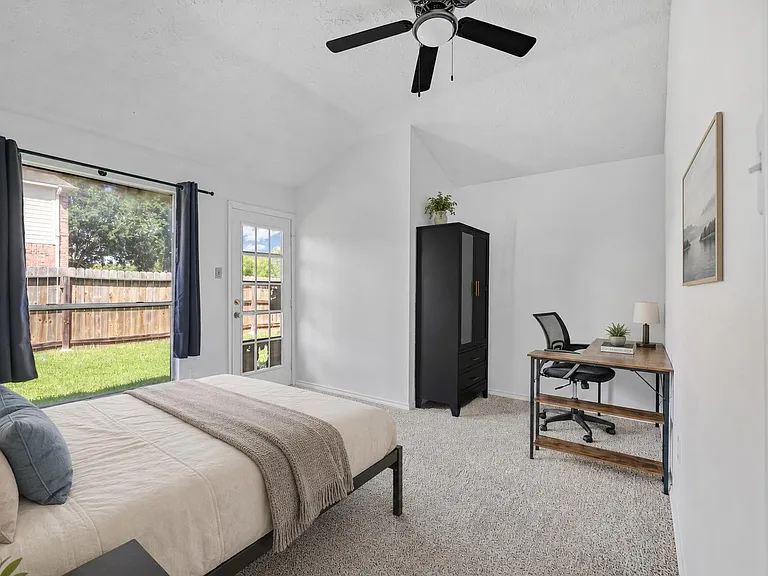 Spacious bedroom with a large window and glass door to the backyard, plus a dedicated desk area and wardrobe storage.