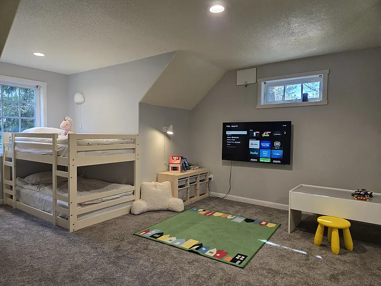 Second-floor kids bedroom with two bunkbeds, play area, toys, books, and a 50" TV