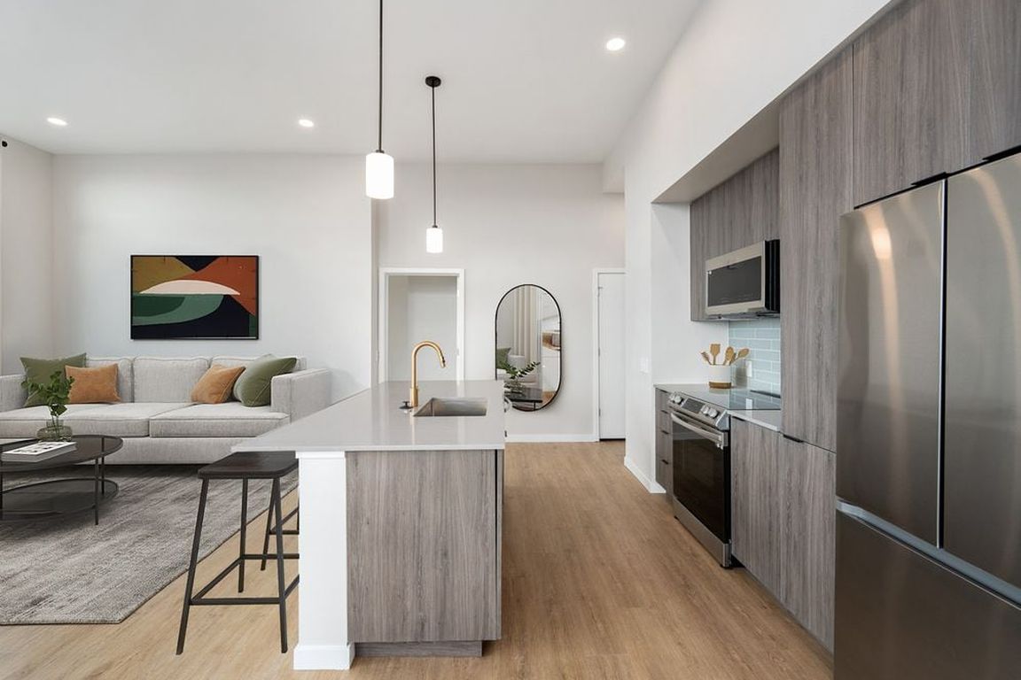 Signature Collection kitchen with dark cabinetry, marbled quartz countertops and backsplash, upgraded stainless steel appliances, and pendant lighting.