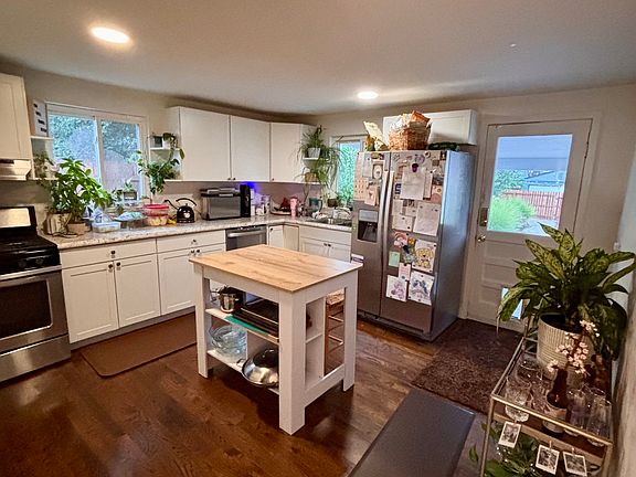 View of kitchen and back door from living room. Kitchen has side-by-side refrigerator with ice maker, newer dishwasher, and gas range and stove.