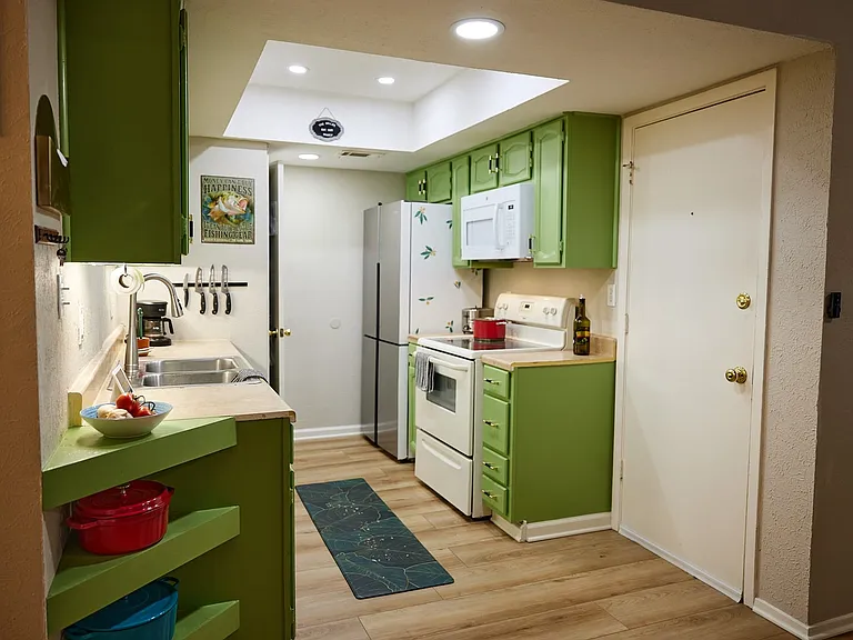 Kitchen featuring green cabinets, white appliances, light wood finished floors, a raised ceiling, and recessed lighting