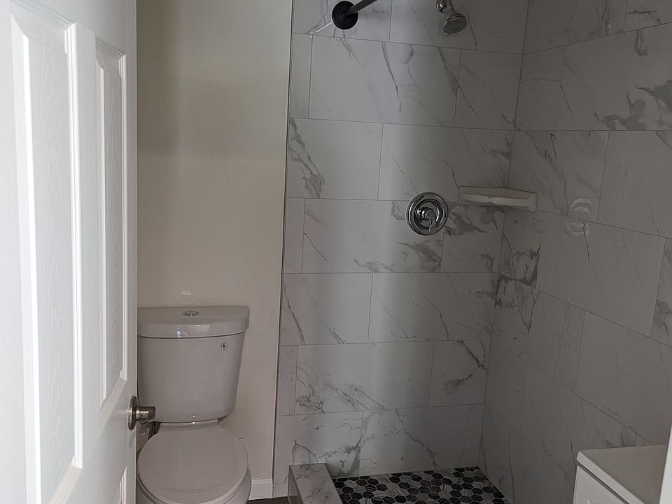 Modern bathroom featuring a custom walk-in shower with floor-to-ceiling marble-style tiling and a curved curtain rod for extra space. Includes a sleek vanity, updated fixtures, and durable hardwood-style flooring for a clean, refreshed look.