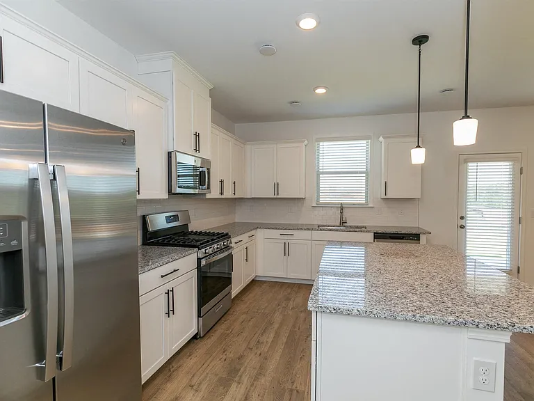 Spacious kitchen equipped with a refrigerator, sink, and ceiling fan leading into the living room