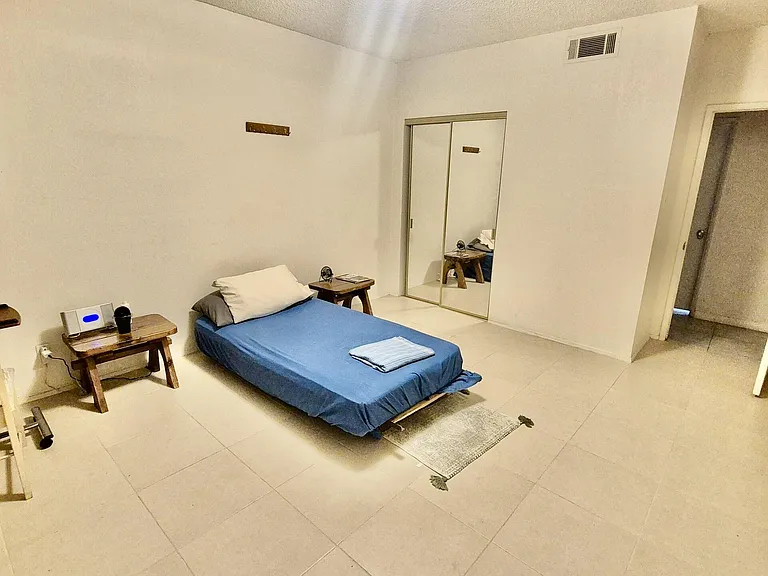 Spacious furnished bedroom with tiled floors, bedside tables, and mirrored closet doors for convenient storage.