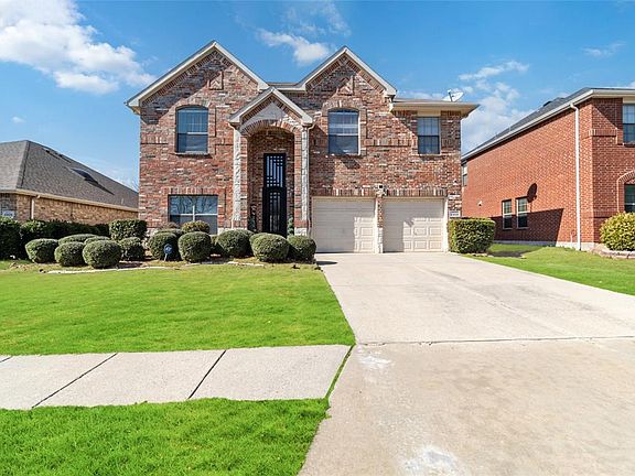 View of front facade featuring brick siding, a front yard, driveway, and an attached garage