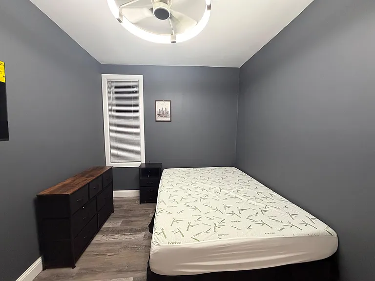 Private bedroom with a full-size bed, dresser, and nightstand, plus a window with blinds and durable wood-look flooring.