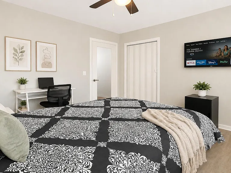 Spacious bedroom with a comfortable bed, work desk, wall-mounted TV, and sliding-door closet for easy storage.