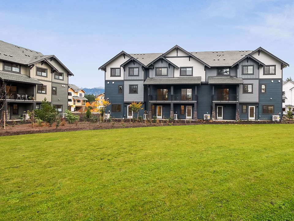 A modern multi-unit residential building with a grassy lawn in the foreground, set against a backdro