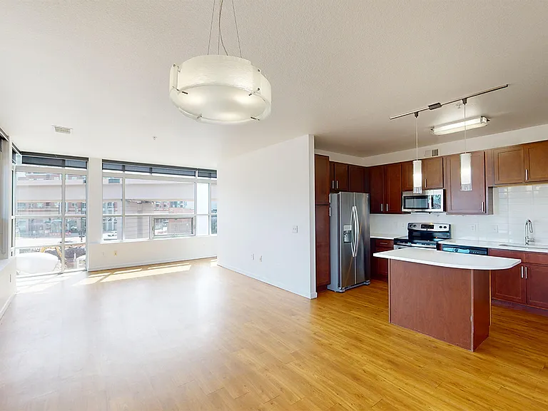 Apartment kitchen with stainless steel appliances, dining and living room with wood-style flooring.