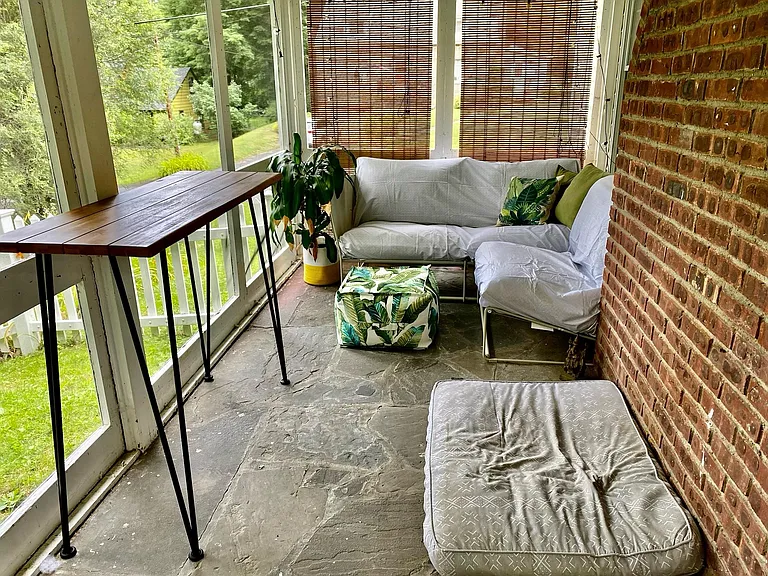 Breezy covered and screened in porch with privacy screens, blue stone floor, and exposed brick.