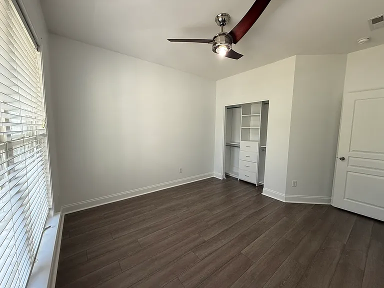 Downstairs bedroom with pristine modern flooring, a large window, and a custom Closets by Design closet system."