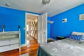 Secondary bedroom with open closet behind door, and dresser. Queen bed. Window facing back garden.