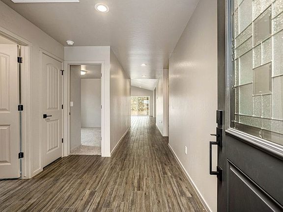A bright hallway with wood-look tile flooring, beige walls, and recessed ceiling lights. White doors