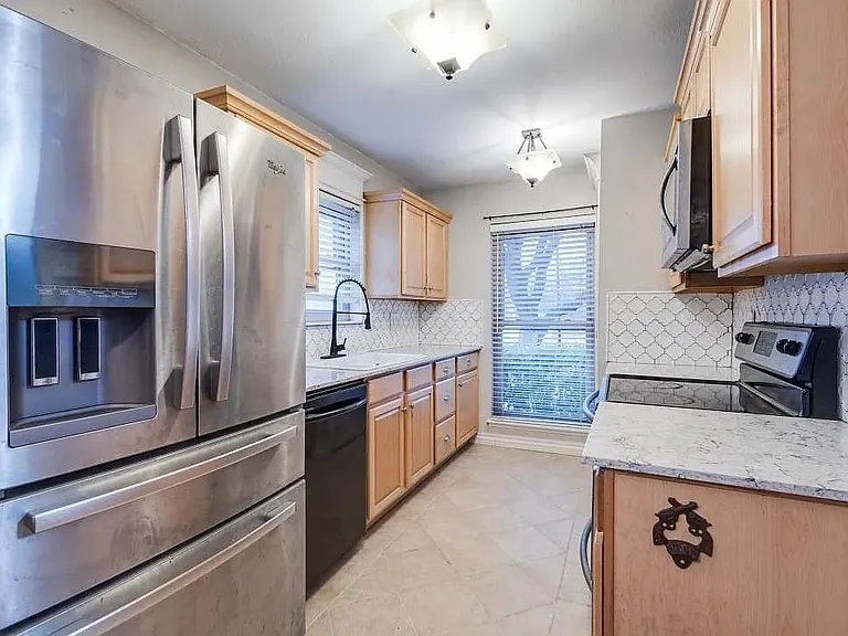 Kitchen featuring stainless steel appliances, light wood cabinetry, white countertops, and a patterned tile backsplash