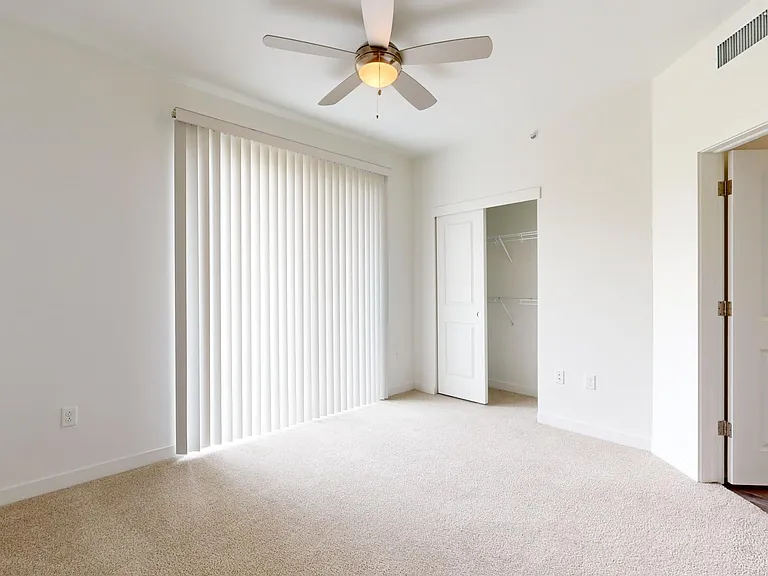 Spacious apartment bedroom with balcony access and plush carpet flooring.