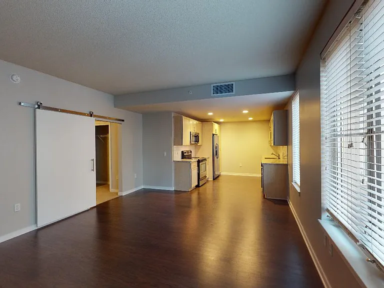 Apartment kitchen with stainless steel appliances, dining and living room with wood-style flooring.
