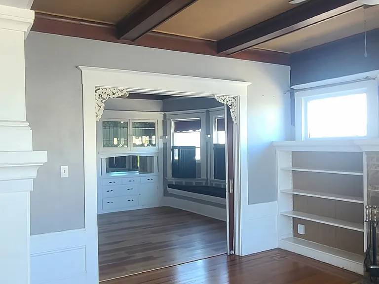 A view into the formal living room and adjacent dining room. Original pocket doors can separate the spaces as needed.