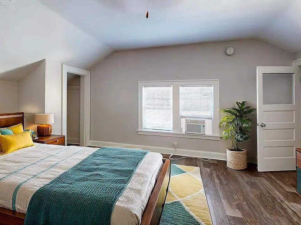 Spacious and inviting bedroom with stylish decor, featuring a cozy bed with vibrant yellow and teal pillows, modern artwork, and lush greenery under natural light.