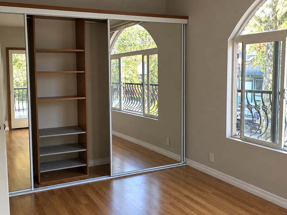 Master bedroom with large arched window facing south and mirrored closet.