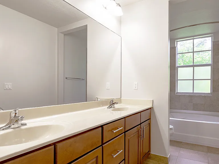Spacious bathroom with dual sinks, natural light, and a full-size tub.