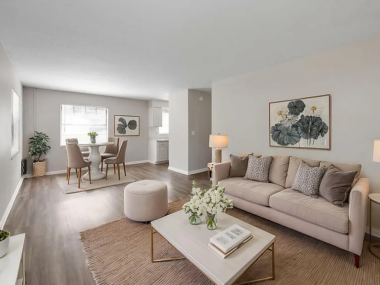 Inviting living room with cozy beige couches, elegant coffee table, and a chic dining area, offering ample natural light and modern decor.